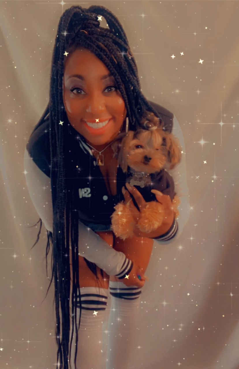 Gia the dog trainer. A smiling woman with braids holds a small dog, both looking cheerful, against a sparkling background.
